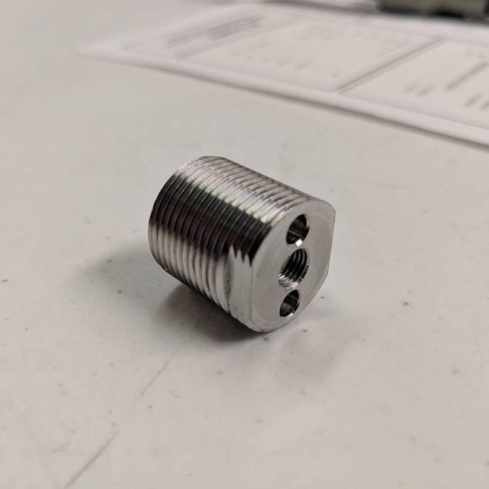 Stainless steel threaded fitting with milled wrench flats and tapped holes.