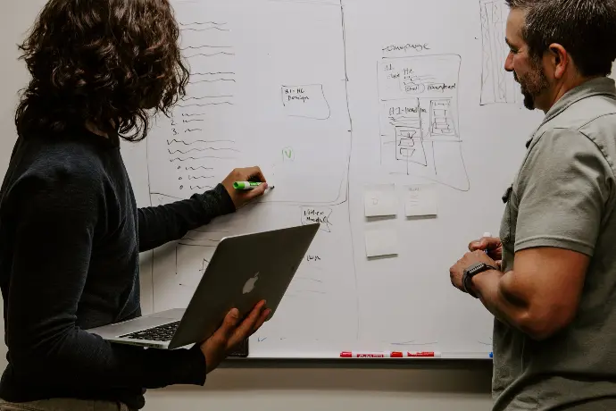 Two people discuss ideas on a wipeboard
